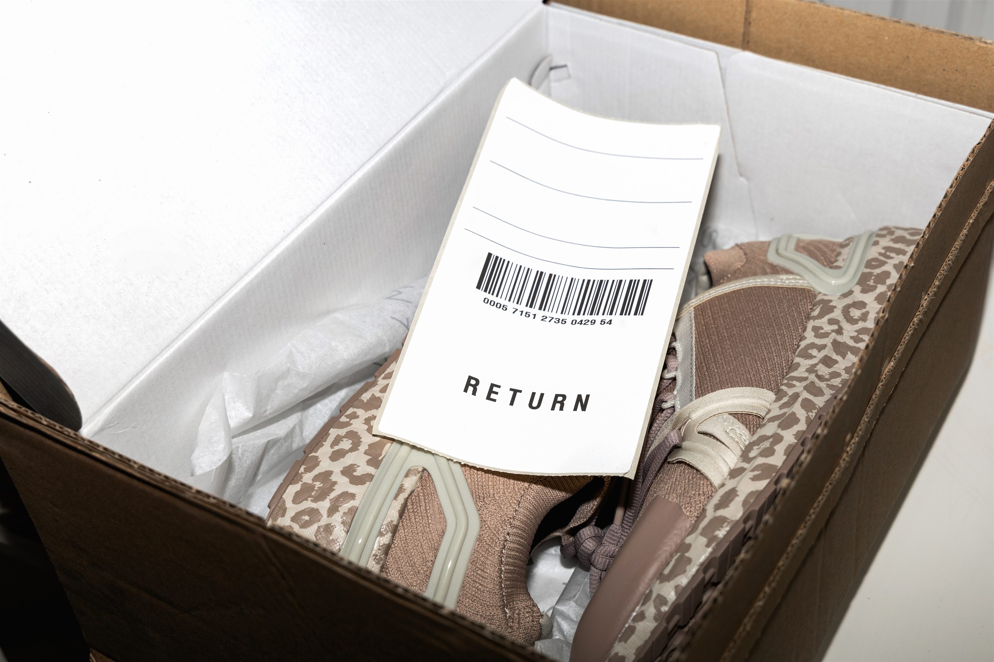 Opened cardboard box holding returned shoes, with a return label on top.